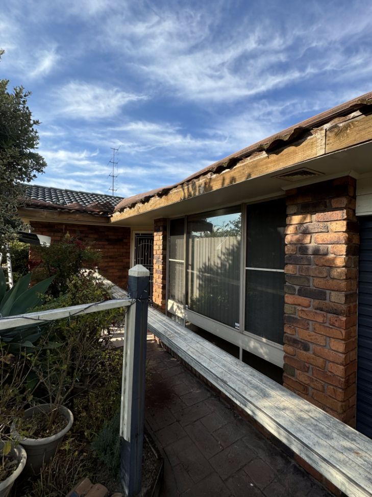 A Brick House With a Wooden Fence in Front of It — Platinum Pride Roofing In Woy Woy, NSW