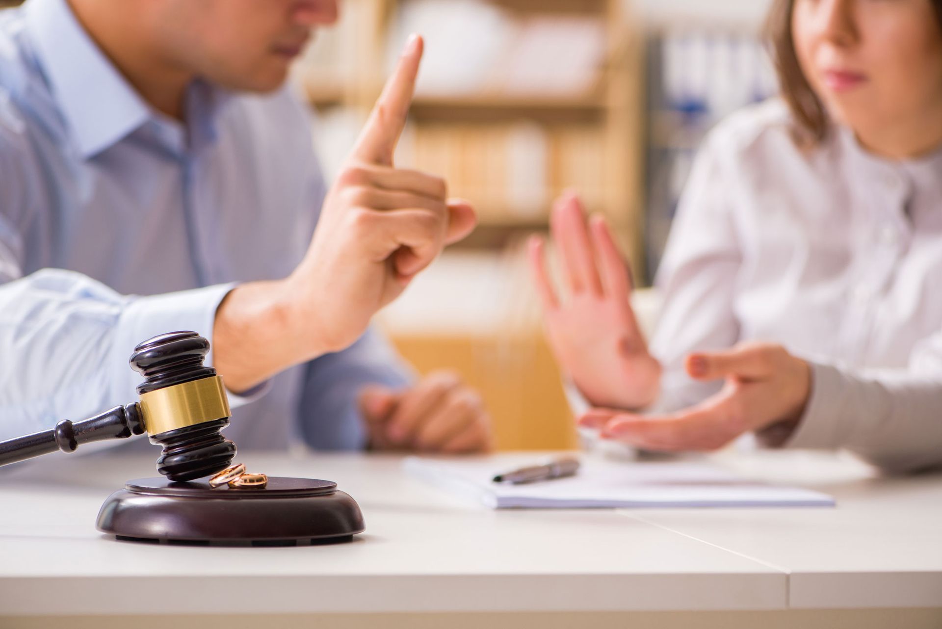 Divorce proceeding: man points finger, woman gestures, gavel and rings on table.