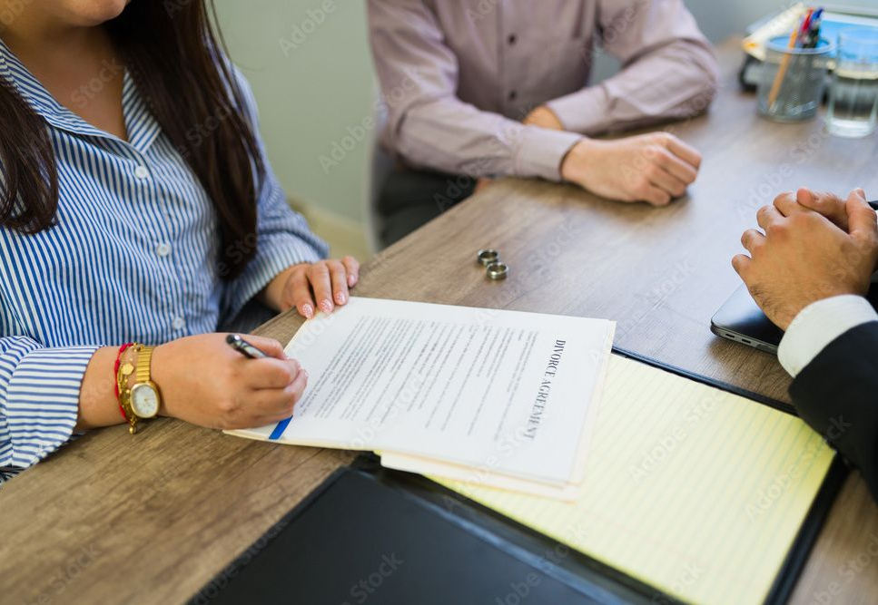 A separation agreement document, pen, glasses, ink stamp, and books on a wooden desk. A separation agreement document, pen, glasses, ink stamp, and books on a wooden desk.