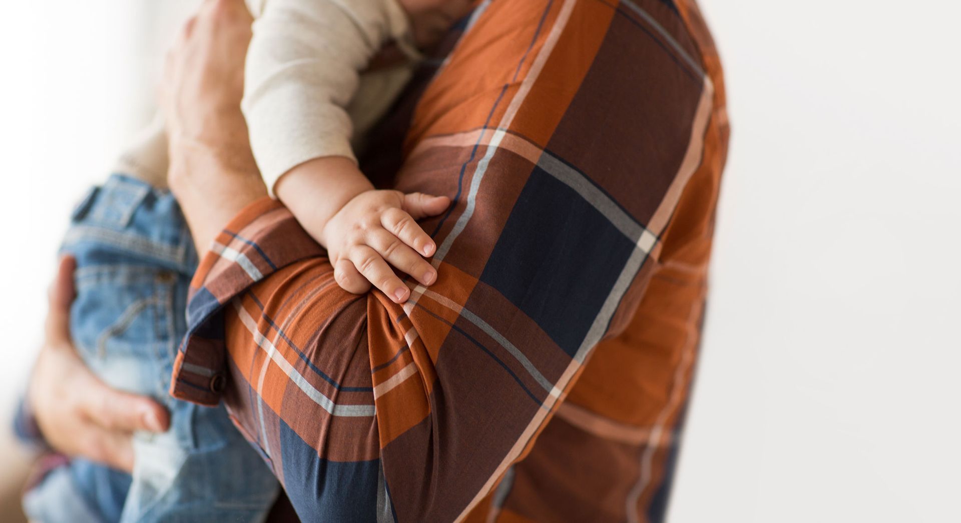 Person holding a baby; plaid shirt, baby's hand on caregiver's arm.