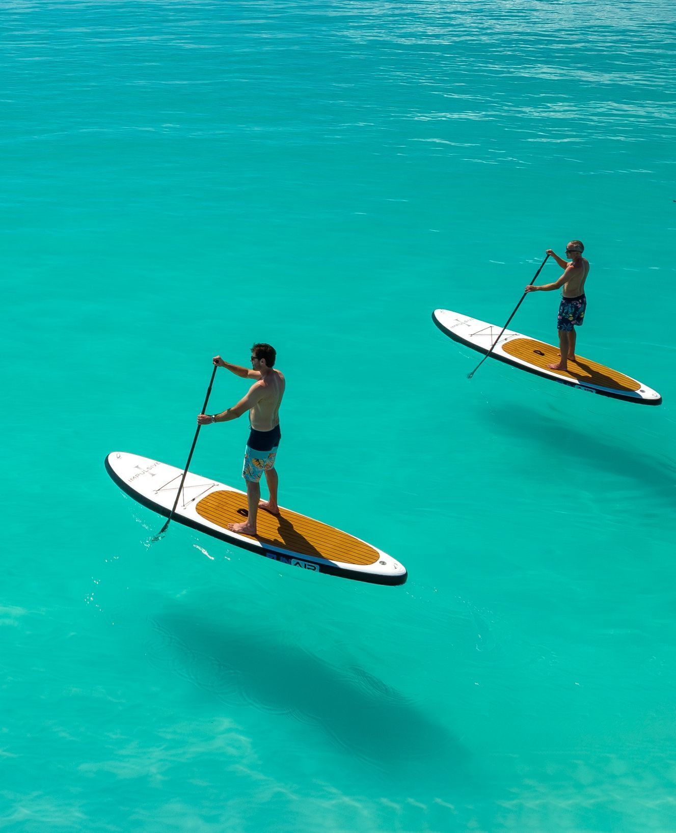A jet ski rider creates a circular wake in bright blue water near a white motor yacht anchored off a forested coast.