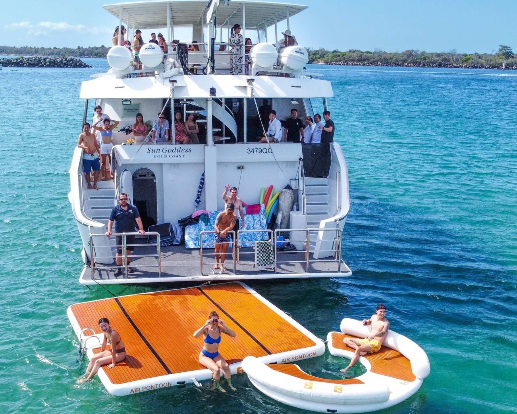 People on a large yacht and floating platforms in sunny, clear turquoise water.