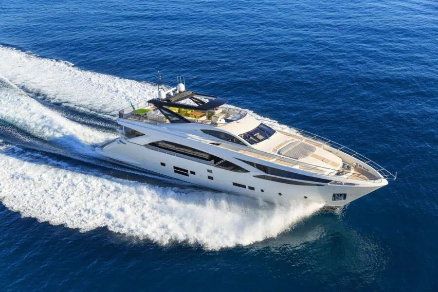 A sleek white luxury motor yacht cruising at speed through deep blue water, leaving a white wake behind it.