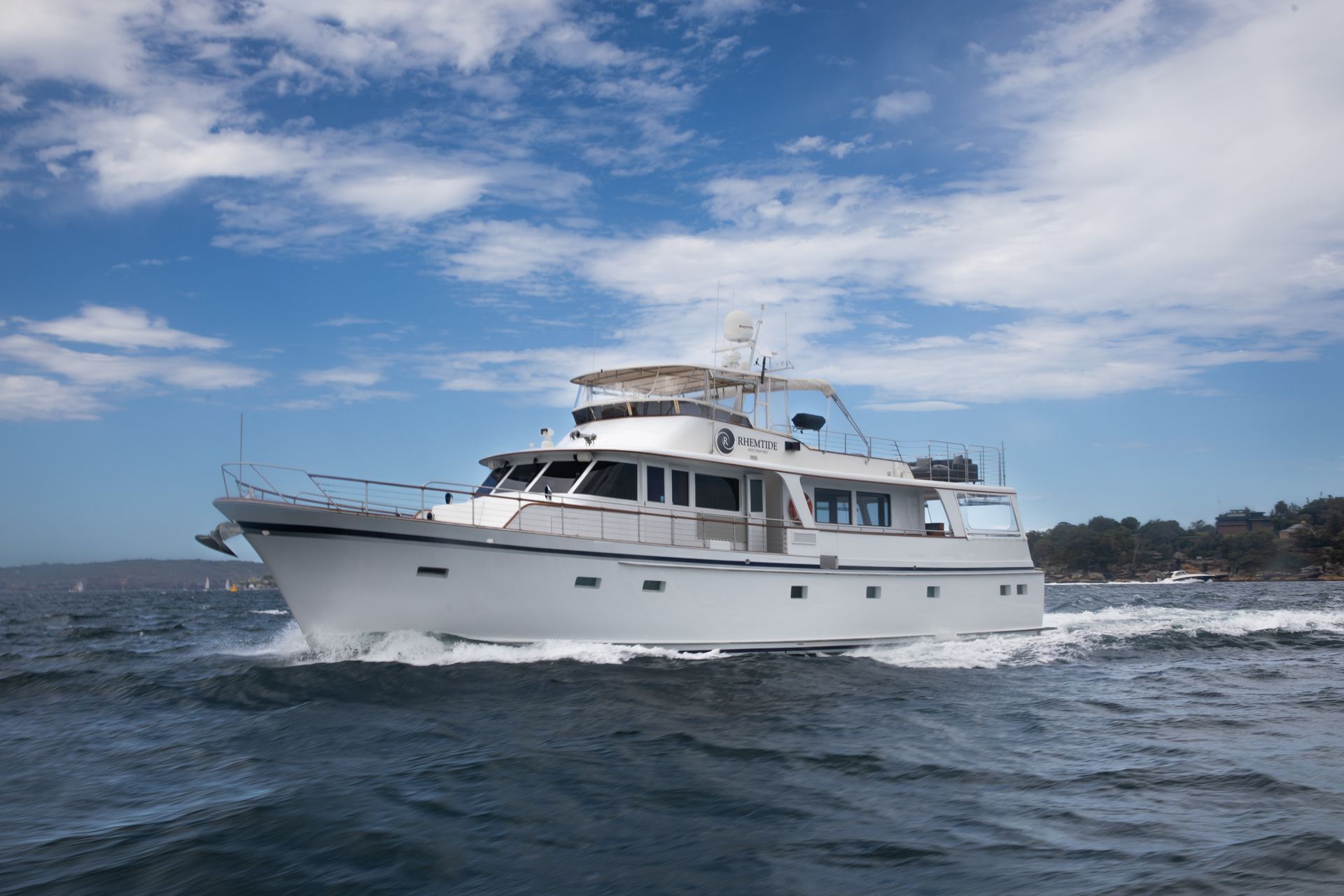 A white motor yacht cruising across blue water under a partly cloudy sky.