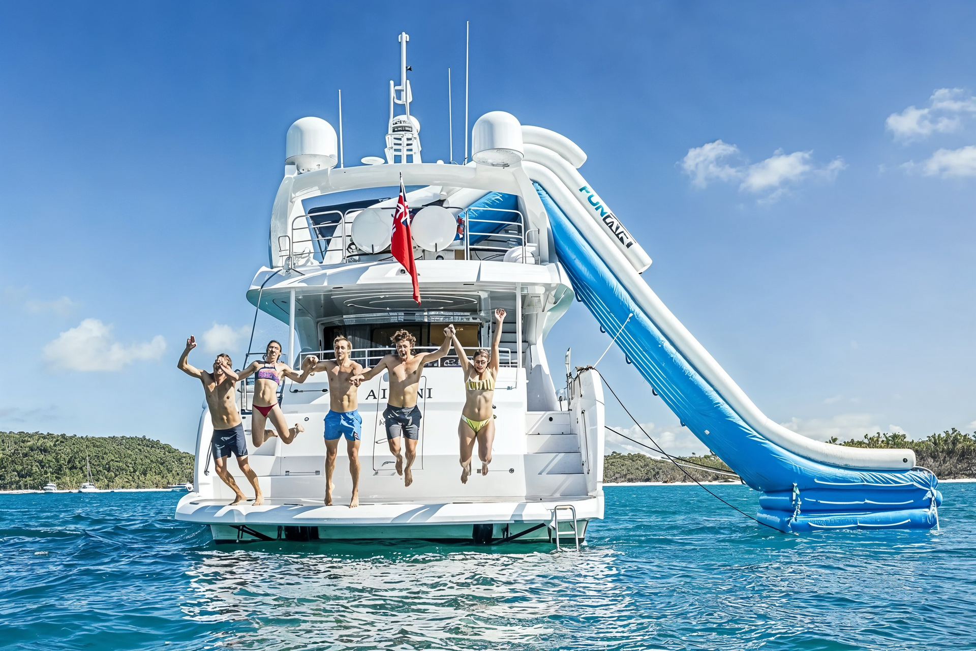 A group jumps off the back of a large white yacht into the ocean, with a blue inflatable slide attached to the side.