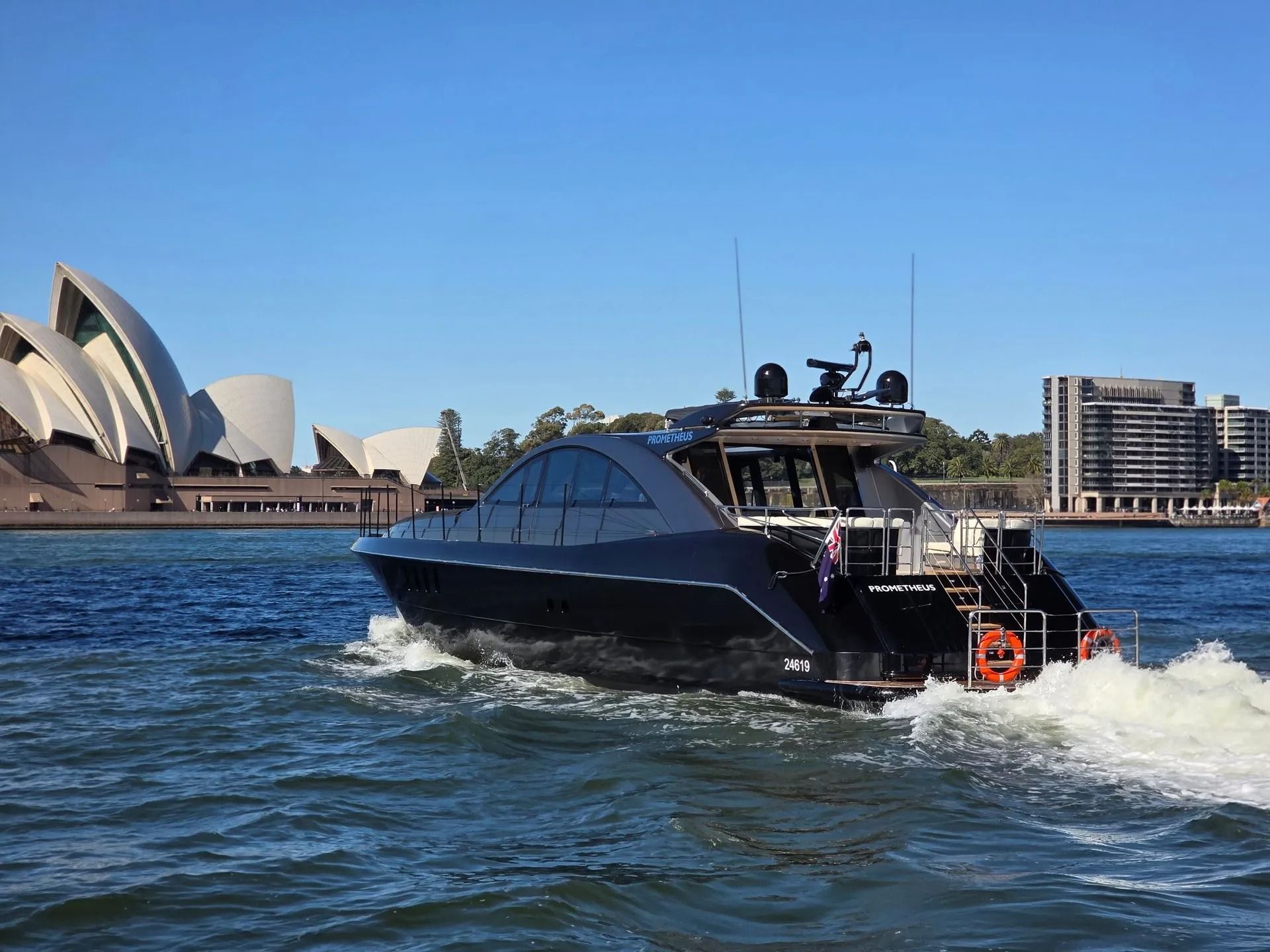 A sleek black yacht cruises past the Sydney Opera House on a sunny day.