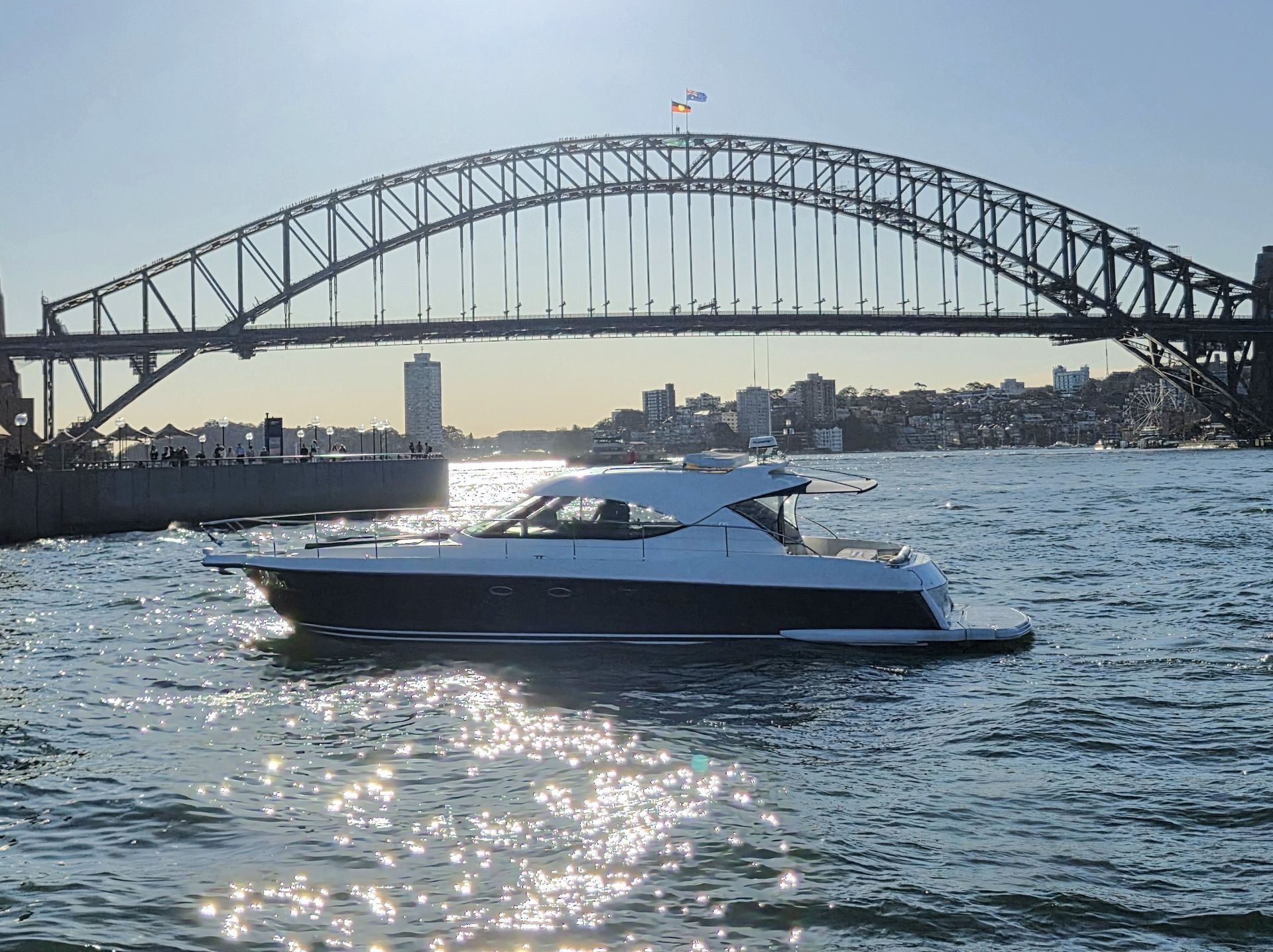 A modern white motor yacht cruising on Sydney Harbour, with the Sydney Harbour Bridge in the background.