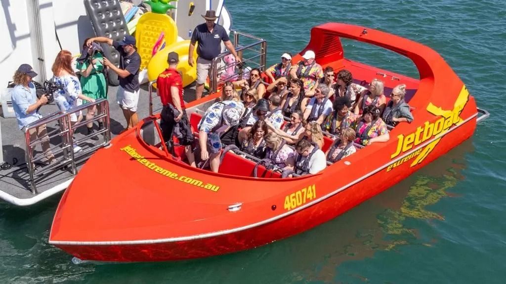 A bright red jet boat filled with passengers docked alongside a pier in blue water.