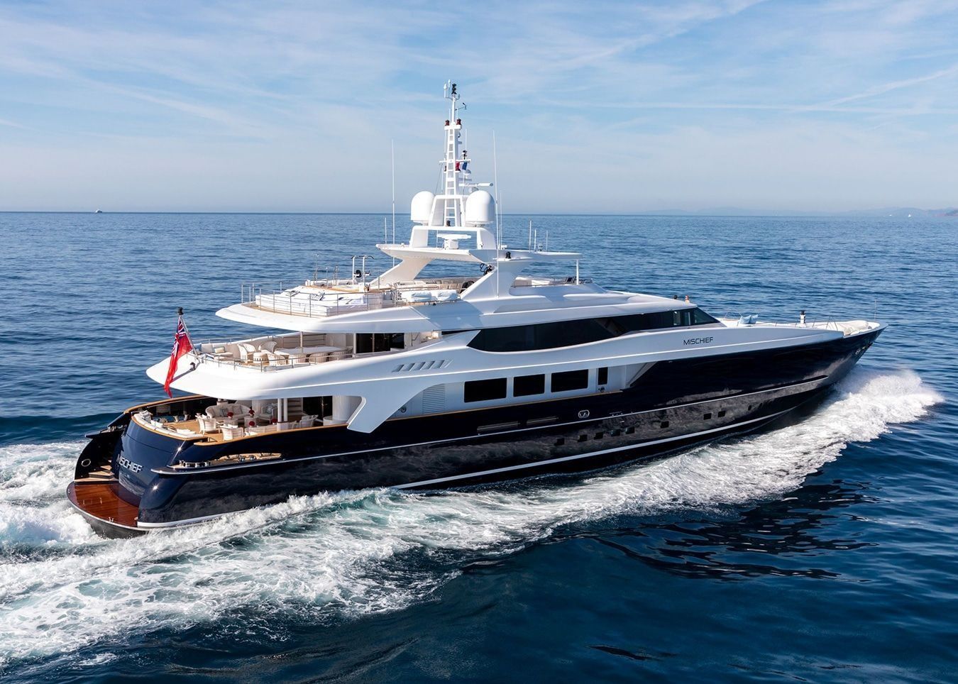 A large, sleek white and dark blue superyacht cruising through open blue water under a clear sky.