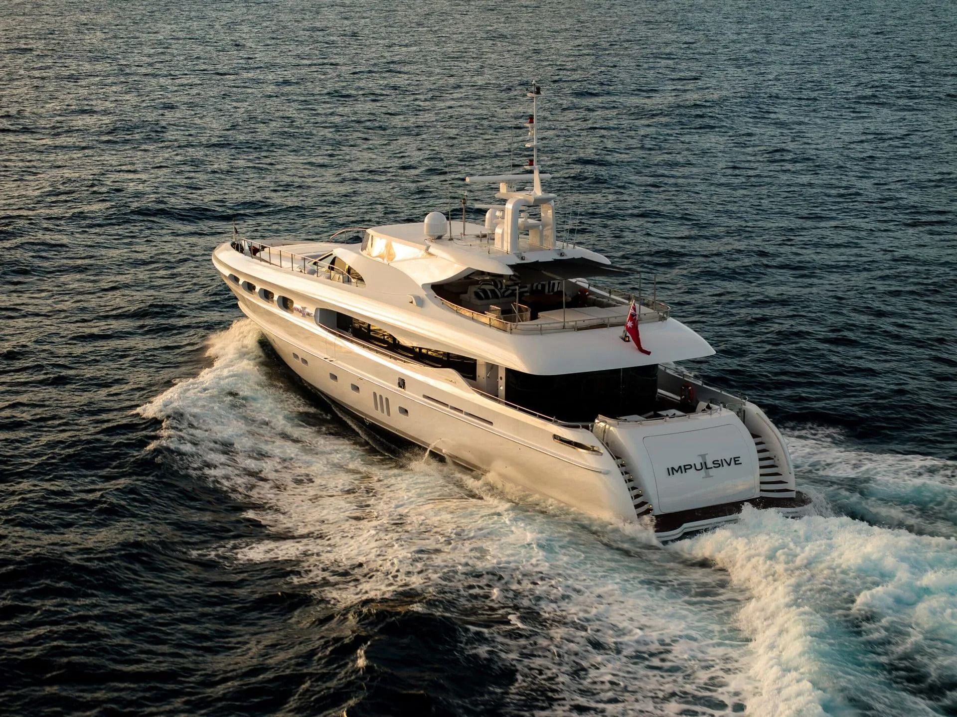 A sleek white superyacht cruises through deep blue water, leaving a prominent wake behind it.