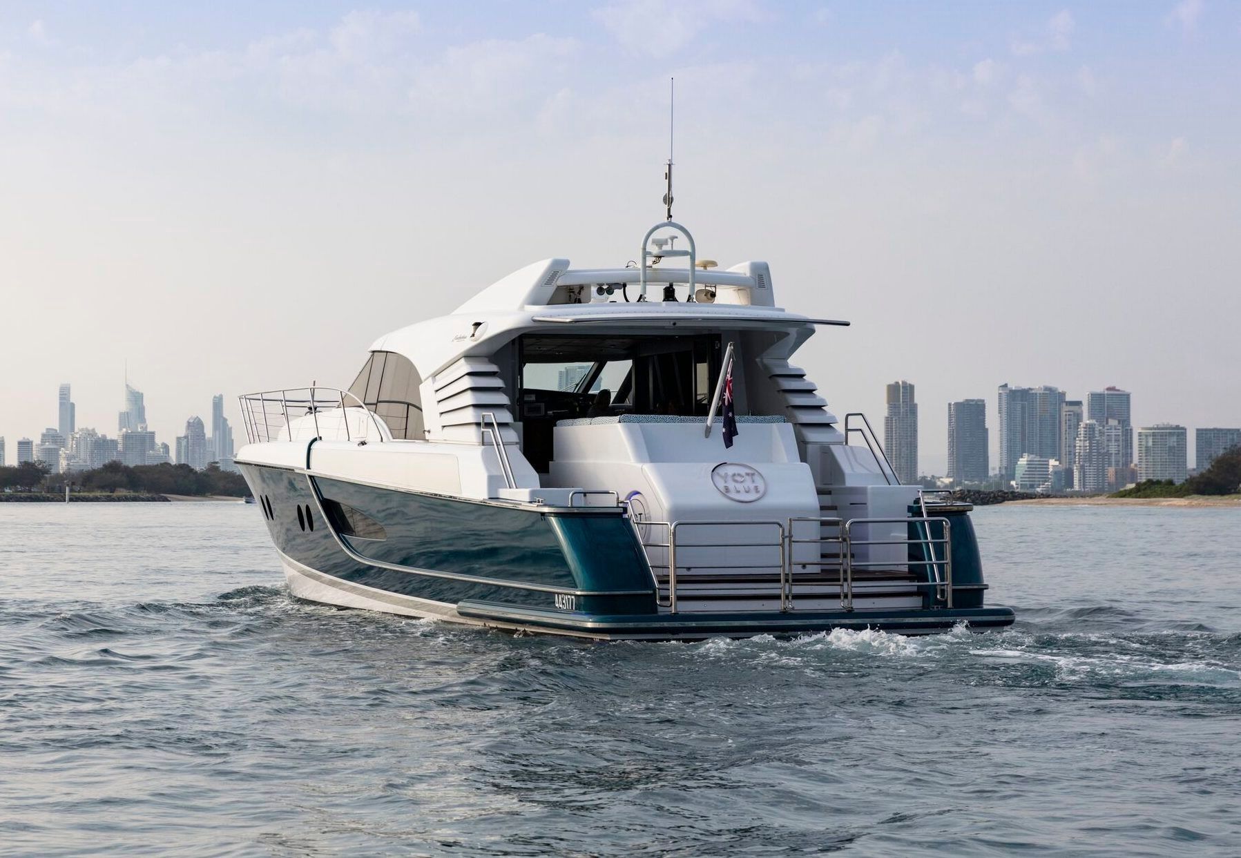 A white and dark teal yacht cruising on the water with a city skyline in the background.