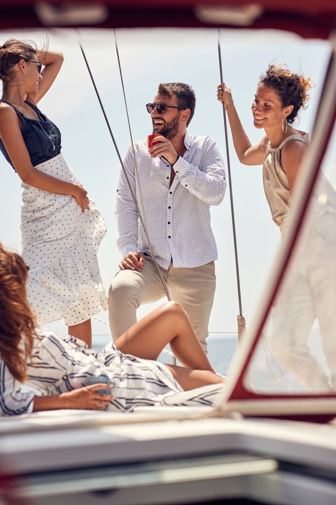 A group of four friends socializing on the deck of a sailboat on a sunny day.