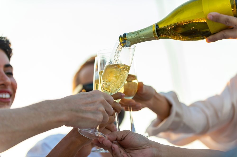 Close-up of hands pouring sparkling wine into multiple champagne flutes held by a group during a celebration.