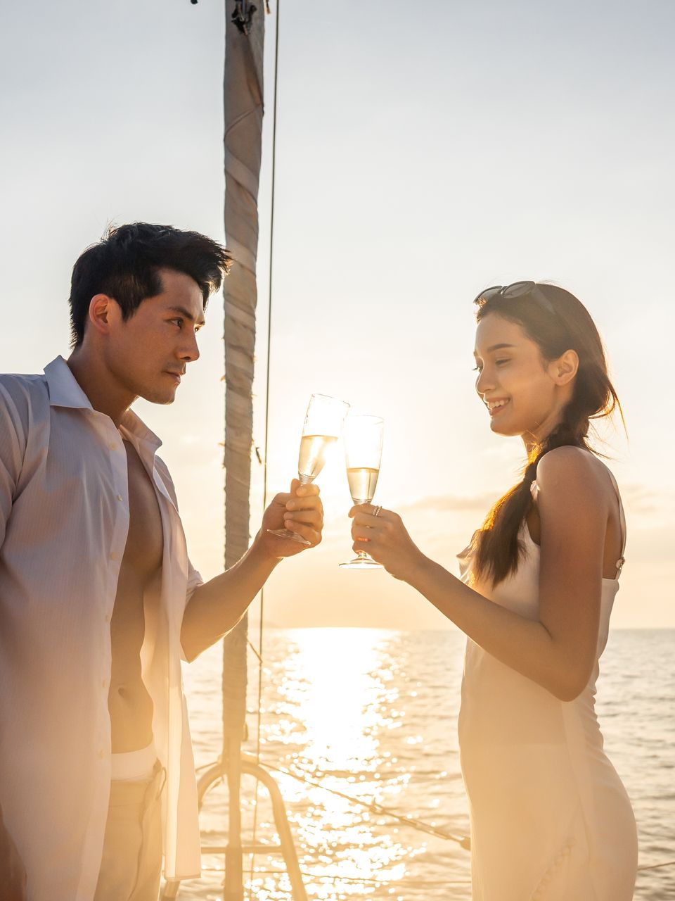 A couple on a boat at sunset, smiling and clinking glasses of champagne together.