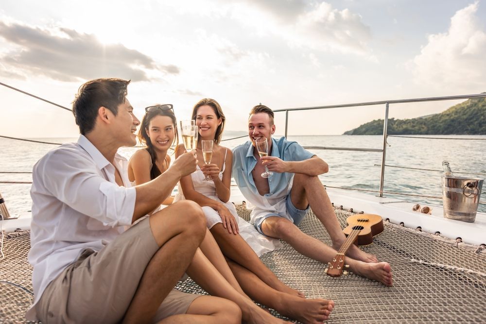 Four people toast with glasses of champagne while relaxing on the deck of a boat at sunset.