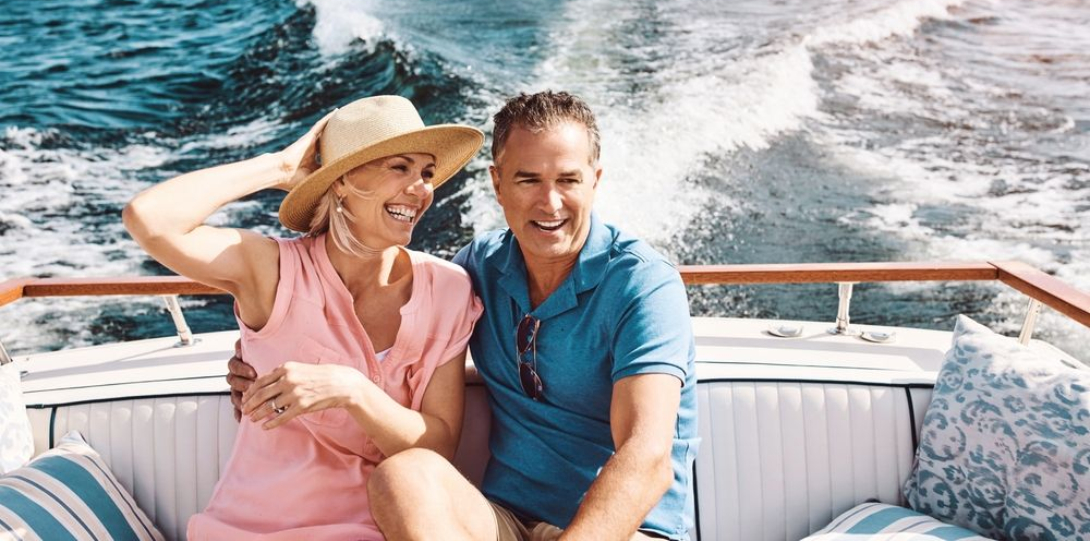 A smiling couple sits together on a boat, enjoying a ride across open water.