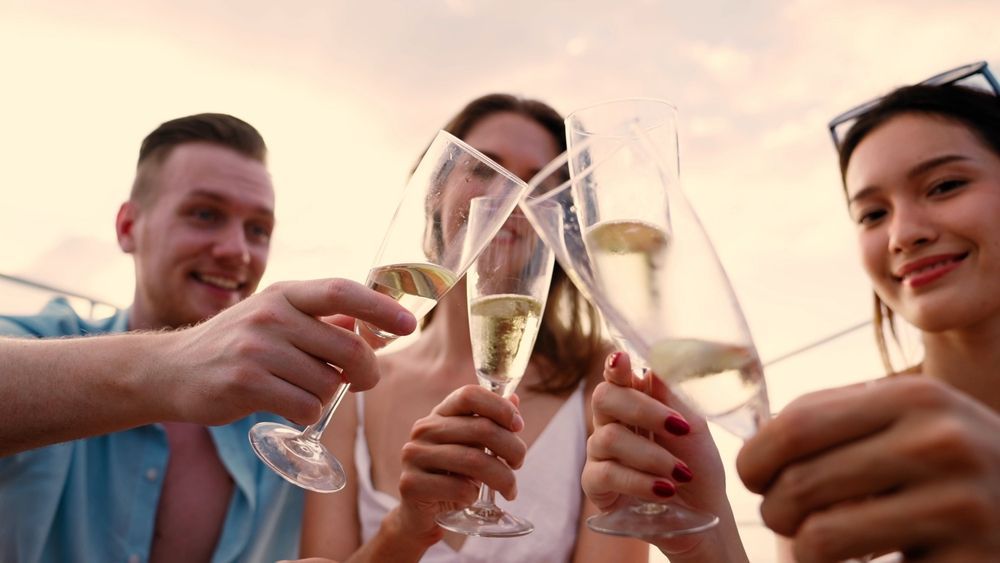 Three people holding up champagne flutes for a toast against a warm, sunset-lit sky.