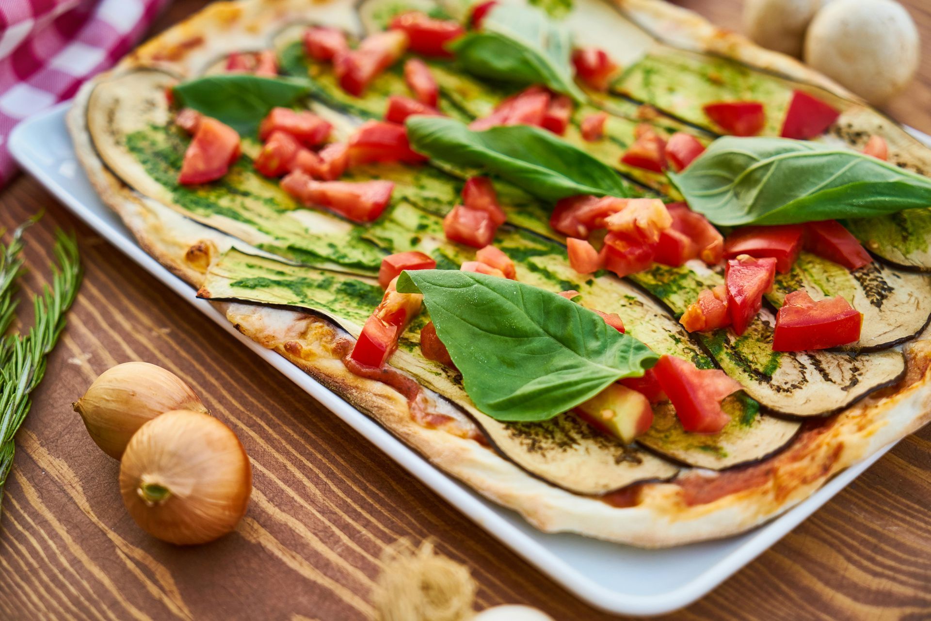 Vegetable flatbread with eggplant, tomatoes, basil, and pesto on a wooden table.