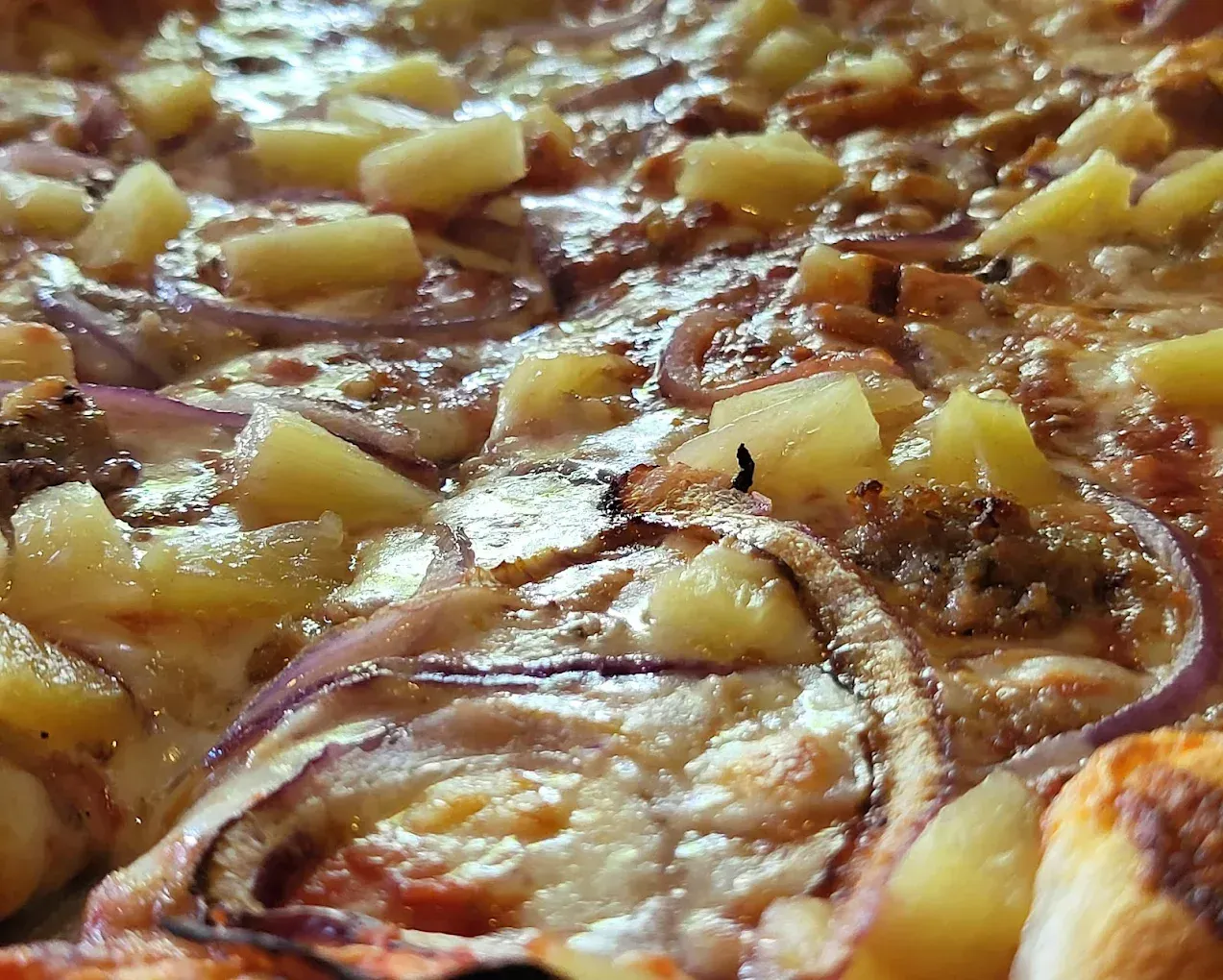 Close-up of a pizza with pineapple chunks, red onion slices, and melted cheese.