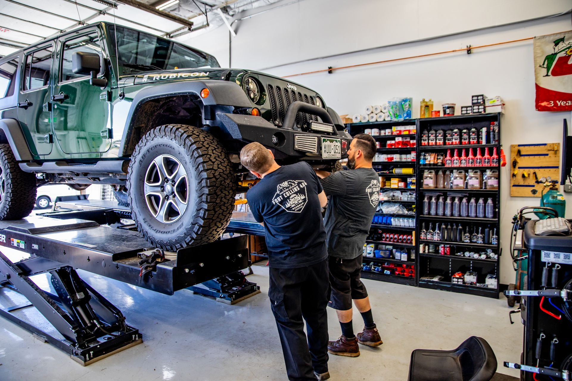 Two mechanics working on a green Jeep in a garage, on a lift | Fort Collins 4x4