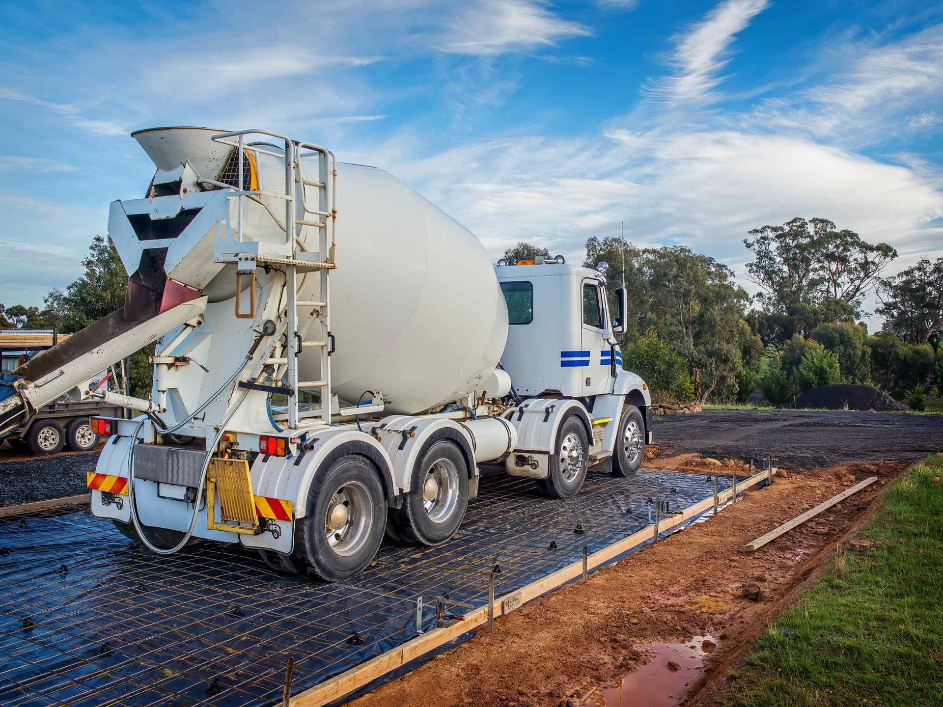 A concrete mixer truck is driving down a dirt road.