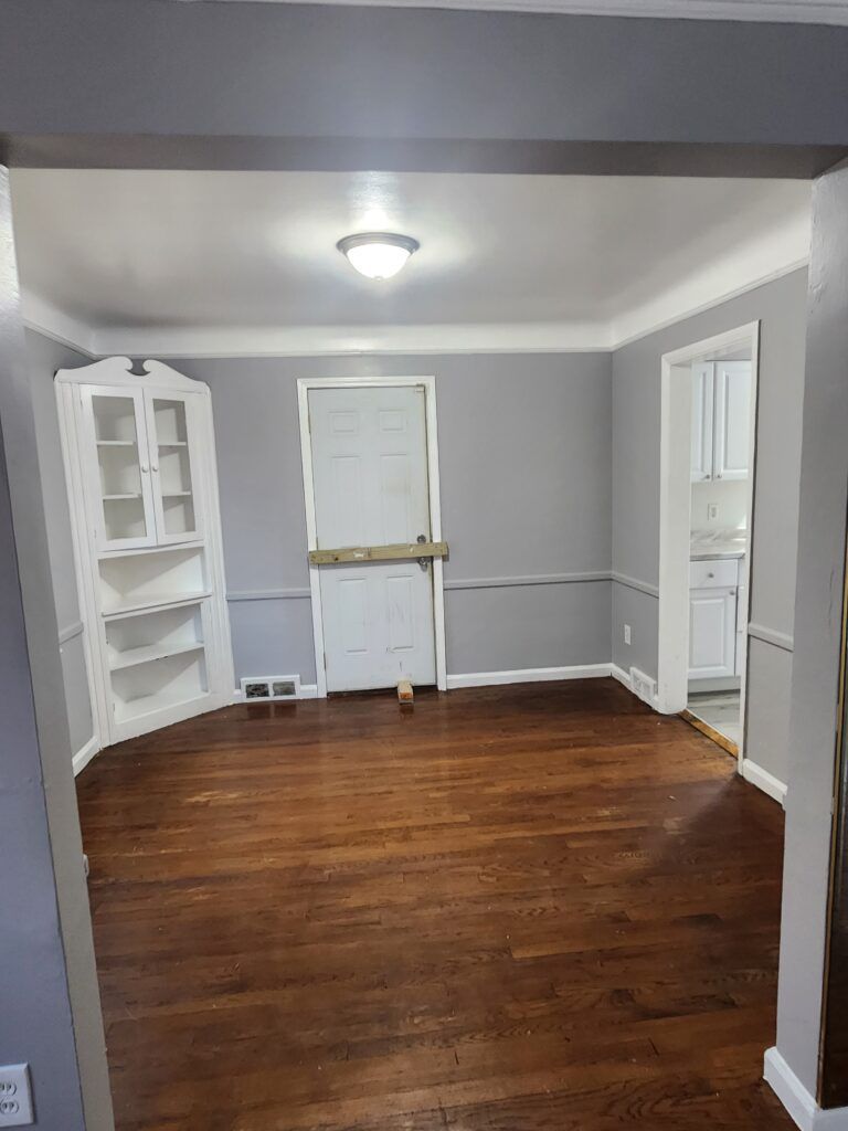 An empty living room with hardwood floors and gray walls.