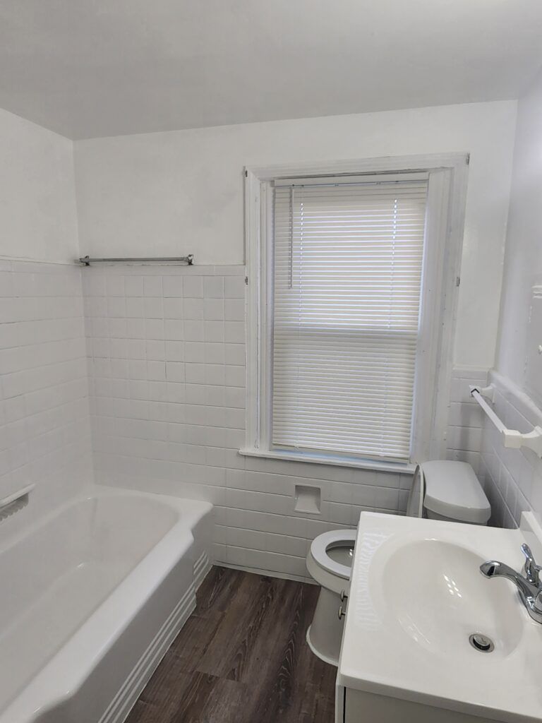 A bathroom with a tub , toilet , sink and window.