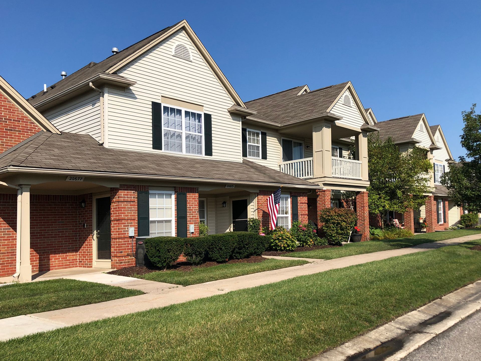 A row of brick houses with white siding and black shutters on a sunny day.