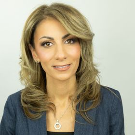 A woman wearing a blue jacket and a necklace smiles for the camera
