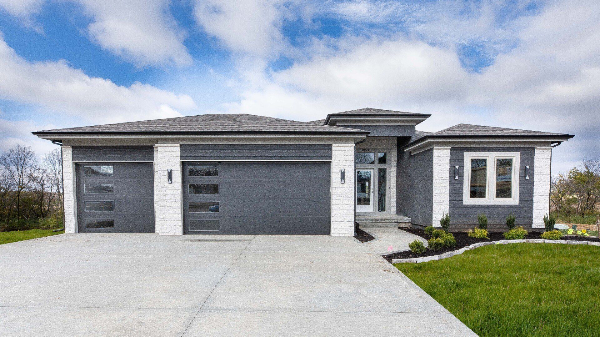 A large gray and white house with two garage doors and a concrete driveway.