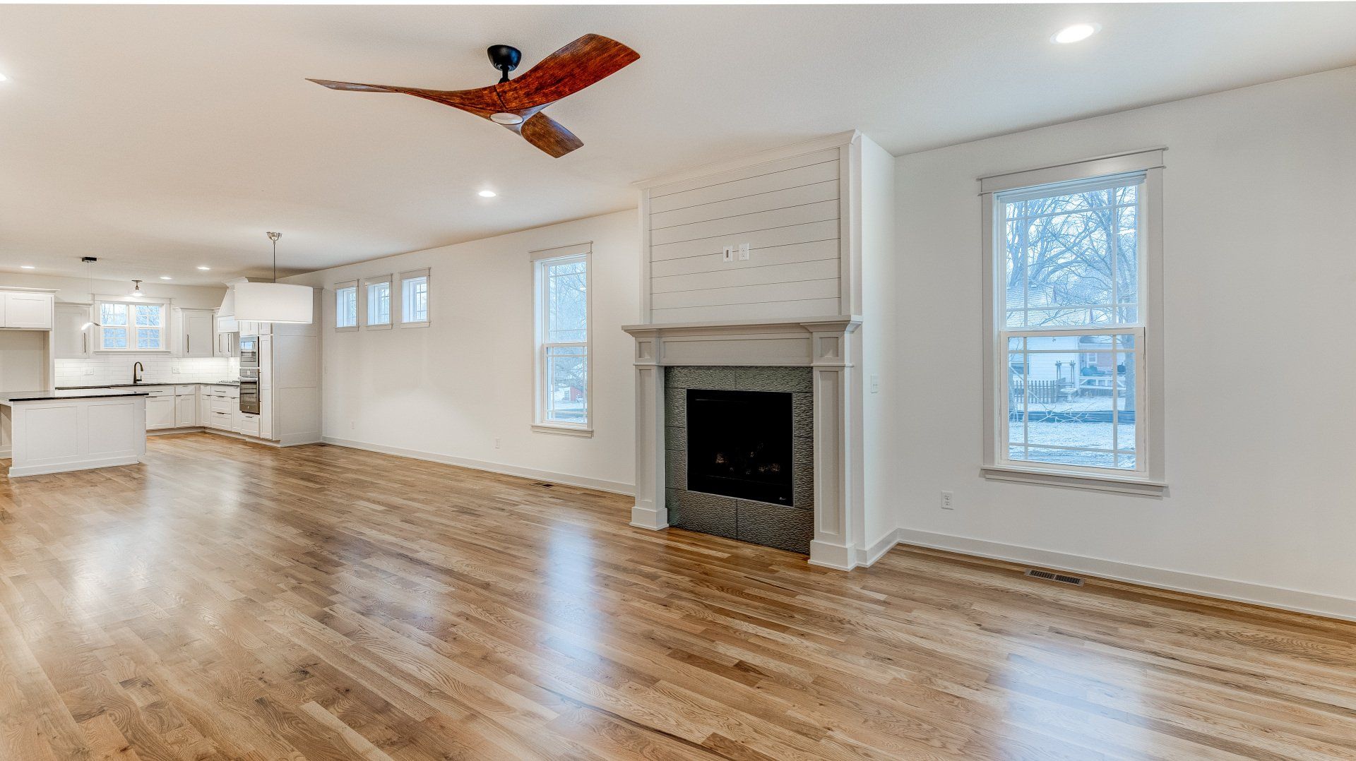 An empty living room with hardwood floors , a fireplace and a ceiling fan.