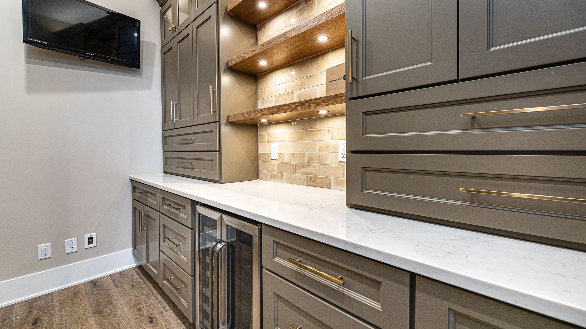 A kitchen with gray cabinets , white counter tops , a refrigerator and a flat screen tv.