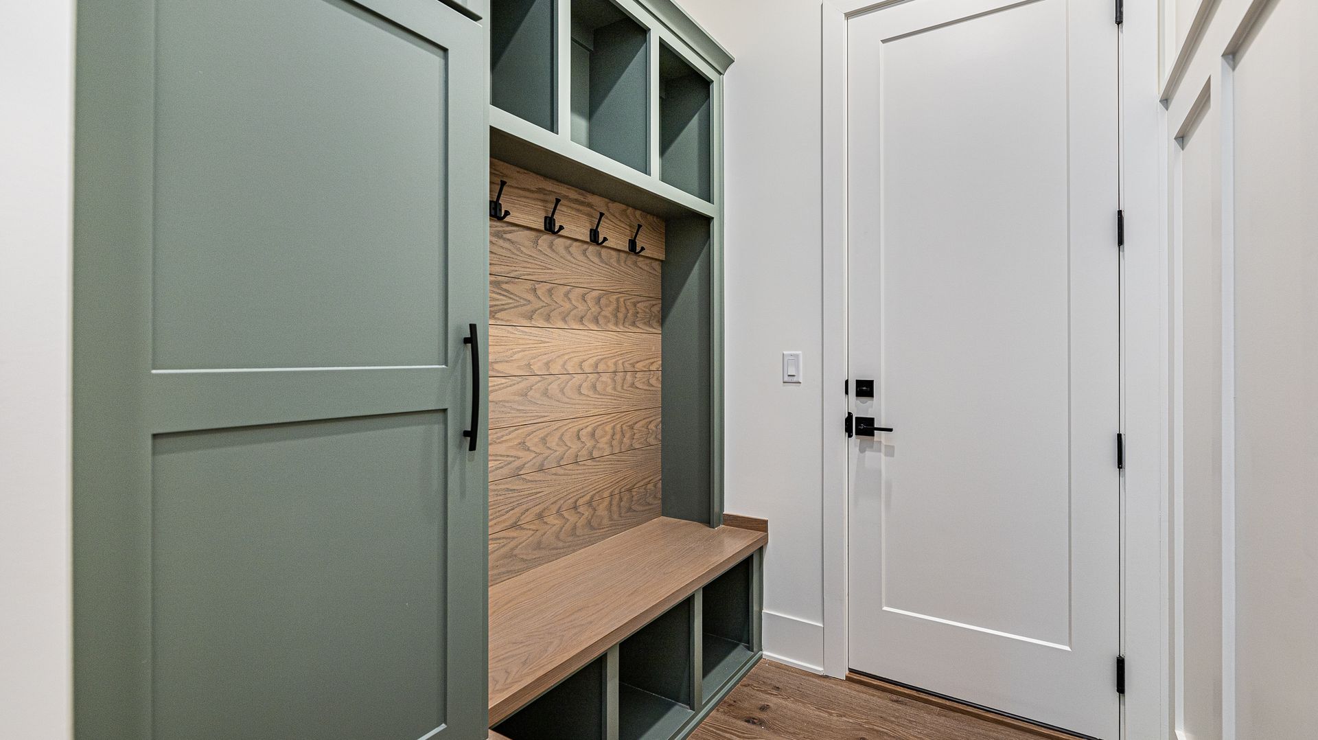 A mud room in a house with green cabinets and a bench.