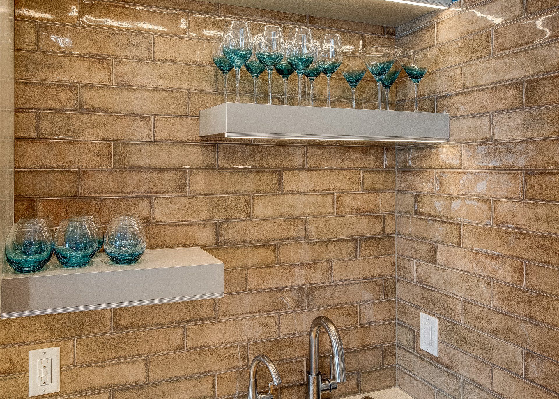 A kitchen with a sink , shelves , and glasses on them.