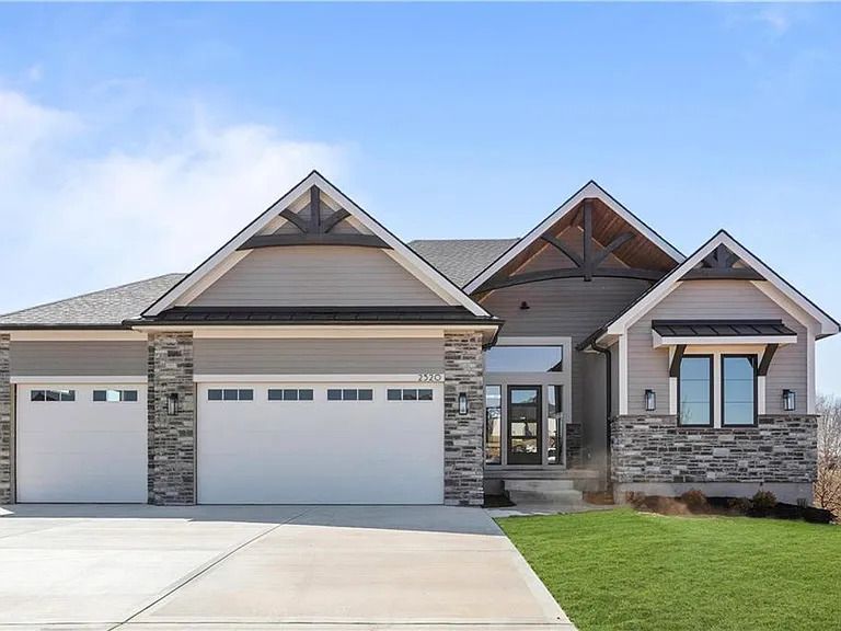 A large house with two garage doors and a stone wall