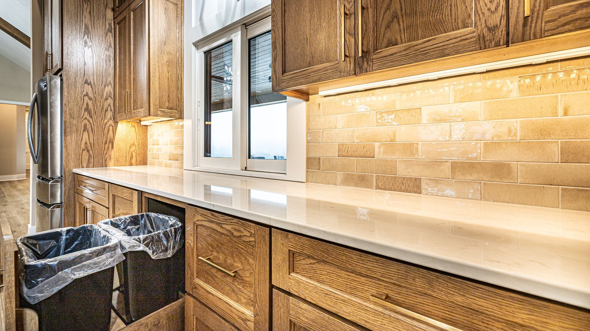 A kitchen with wooden cabinets , white counter tops , and a window.