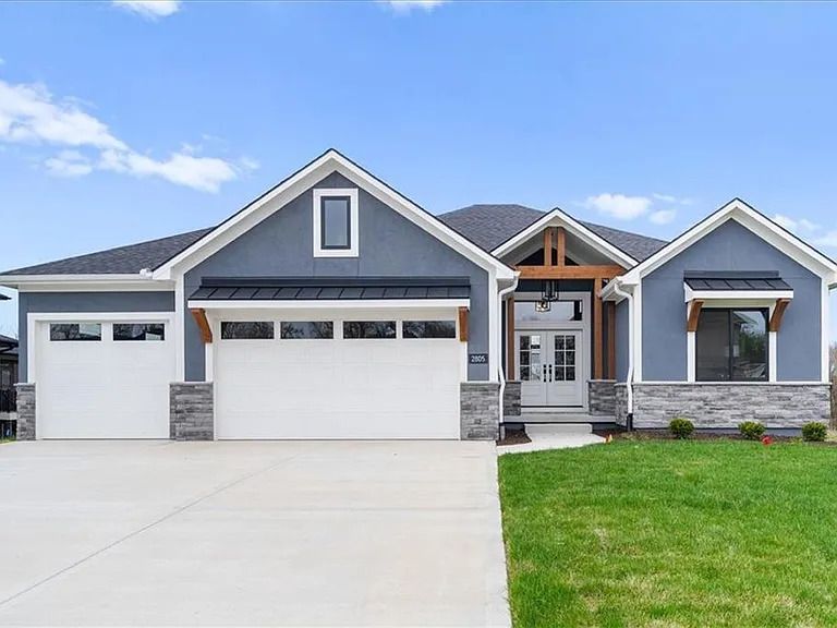 A large gray house with a white garage door and a large driveway.
