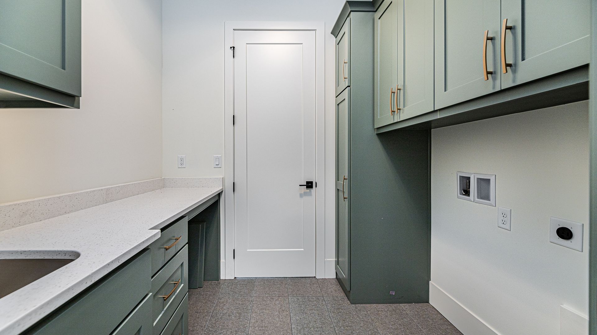 A laundry room with green cabinets , a sink , and a door.