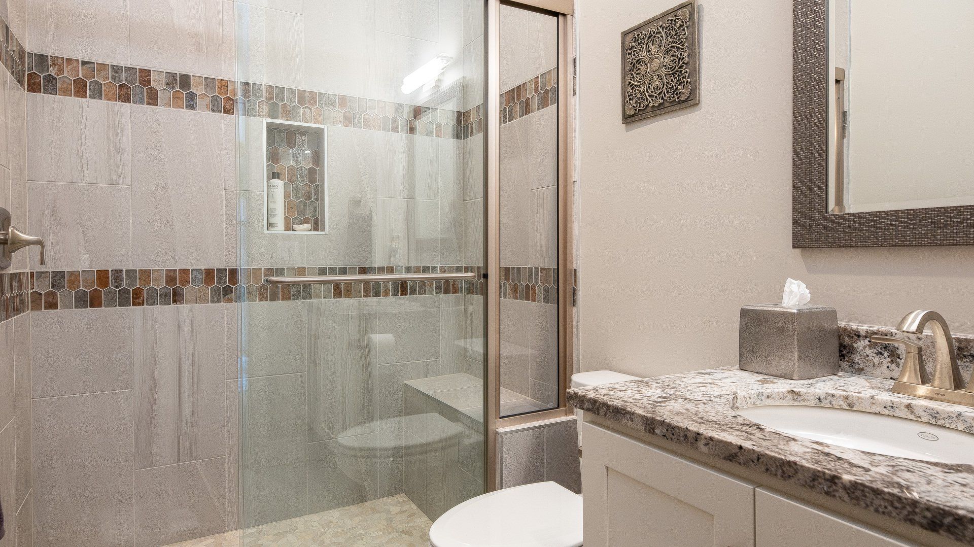 A bathroom with a toilet , sink , mirror and walk in shower.