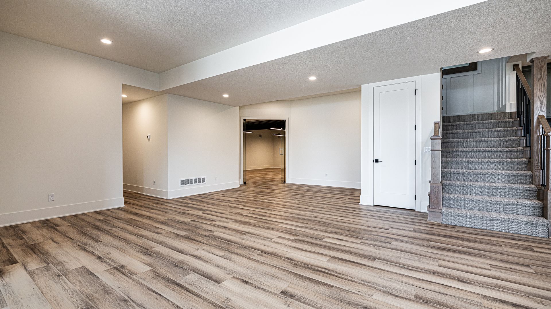 An empty basement with hardwood floors and stairs.