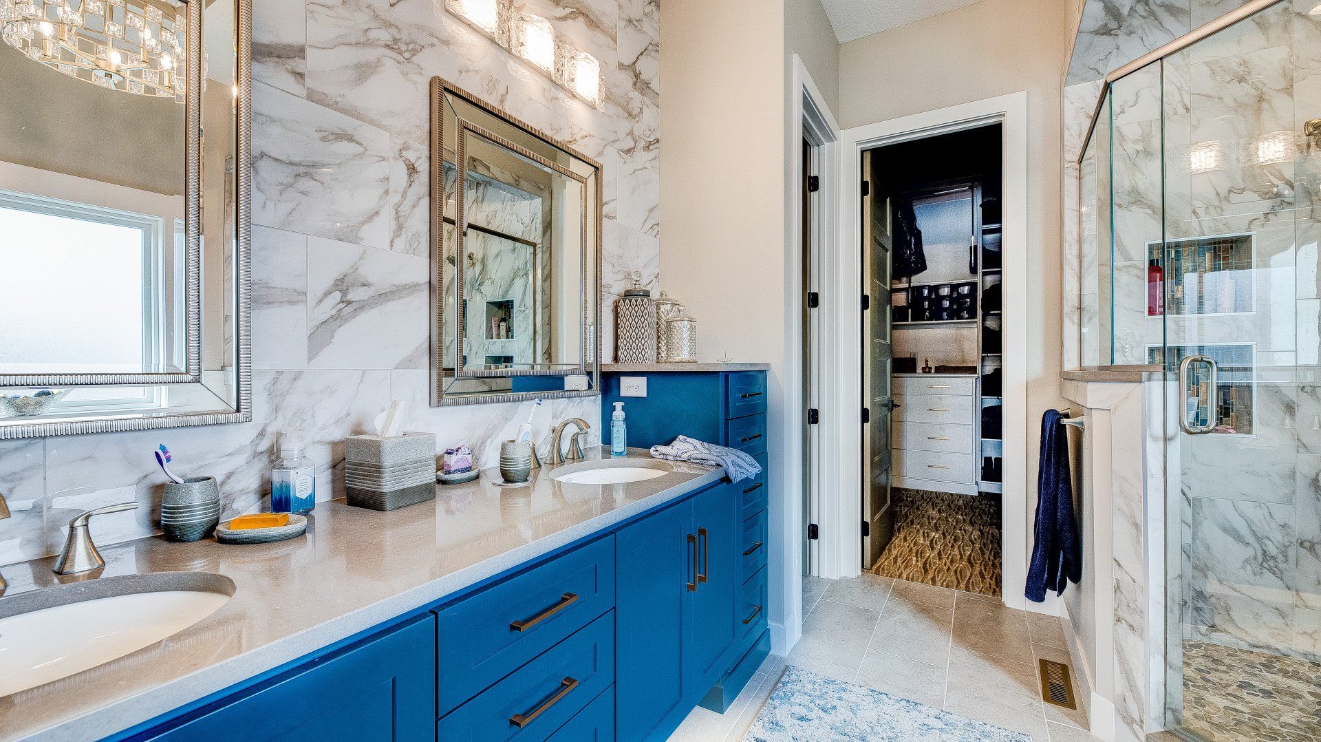 A bathroom with blue cabinets , a sink , a mirror and a walk in shower.
