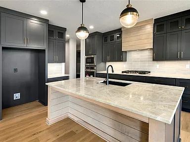 A kitchen with black cabinets , white counter tops , and a large island.