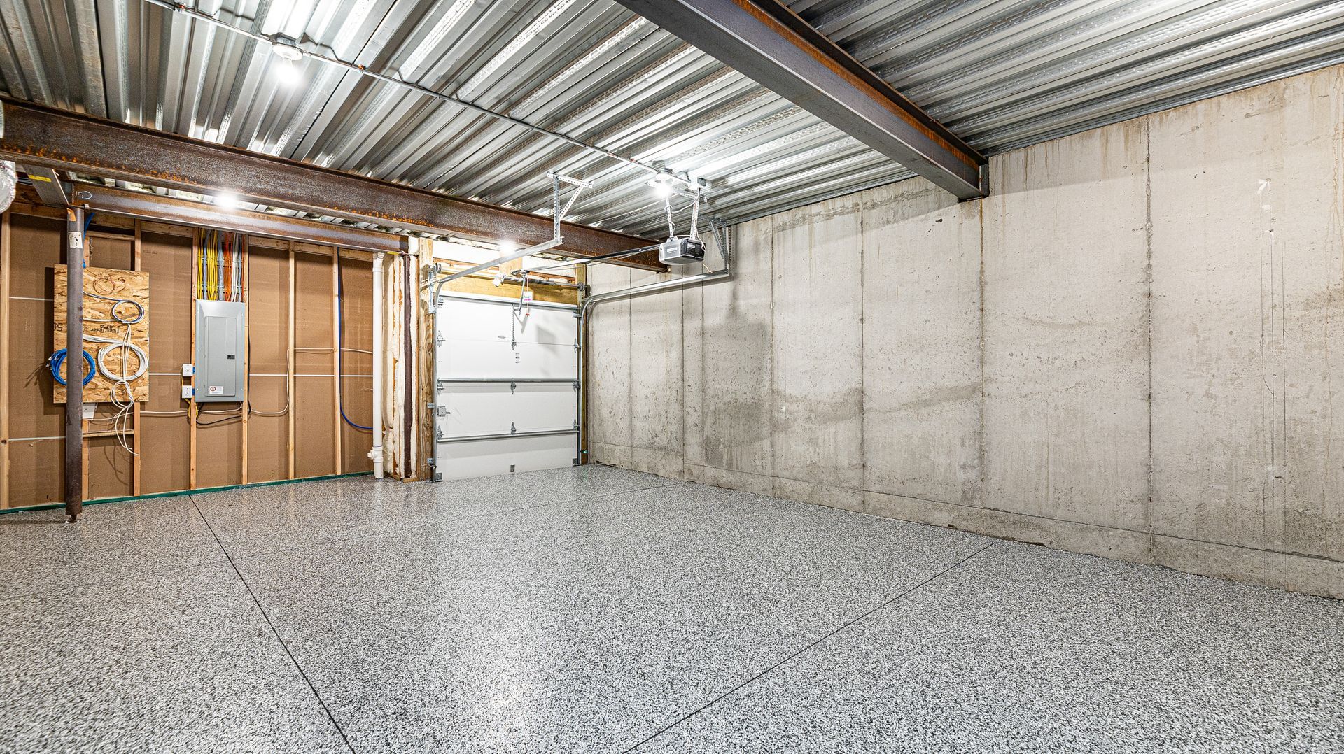 An empty basement with a garage door and a metal ceiling.