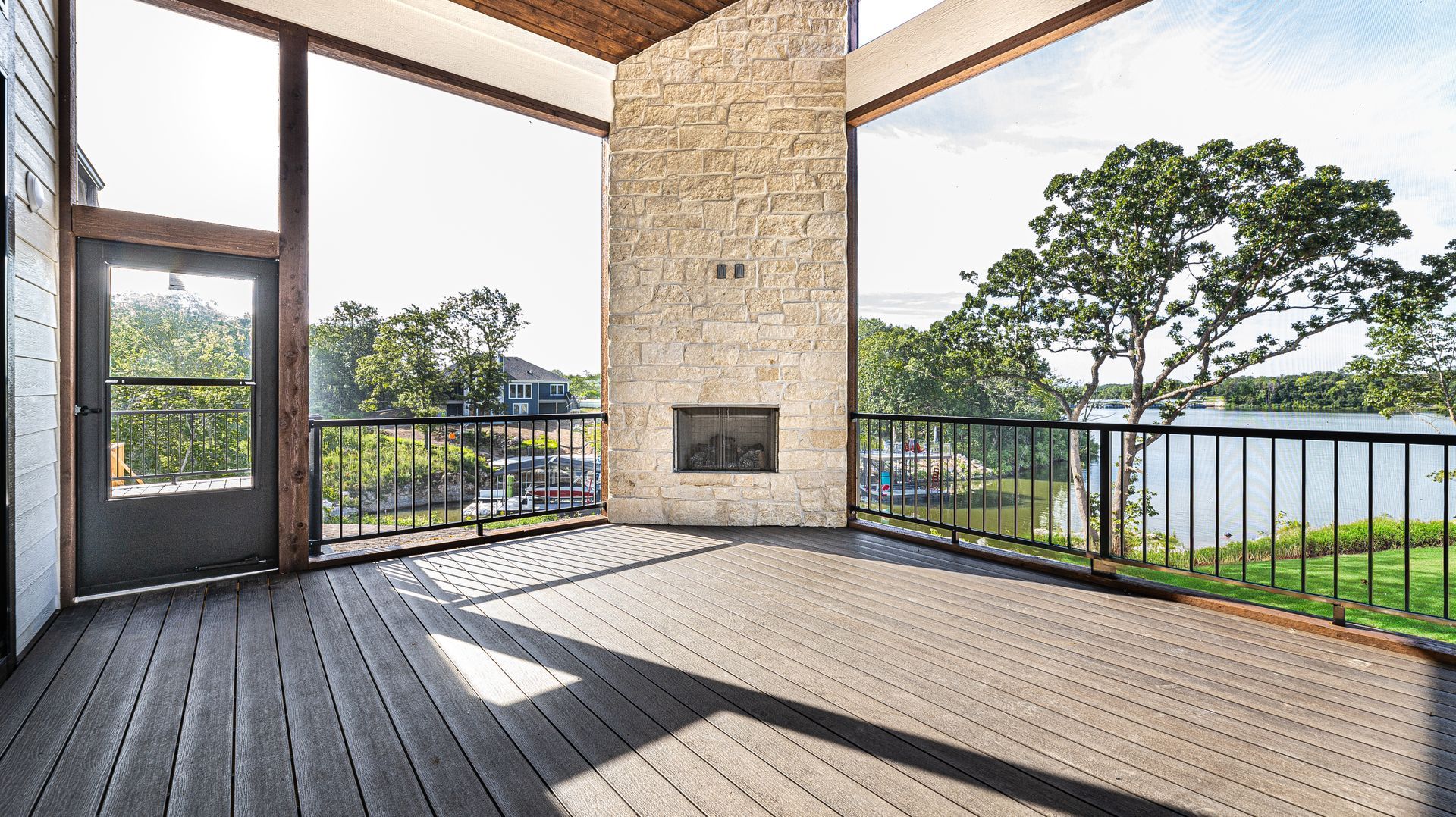 An empty deck with a fireplace and a view of a lake.