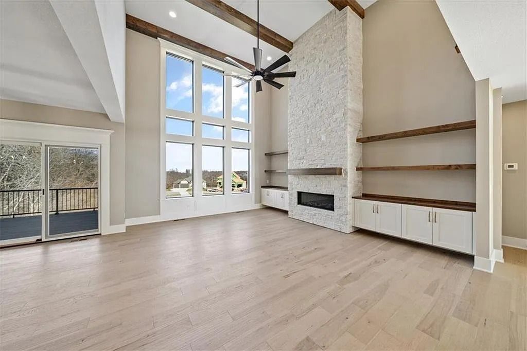 Spacious living room with large windows, fireplace, built-in shelves, hardwood floors, and deck access.