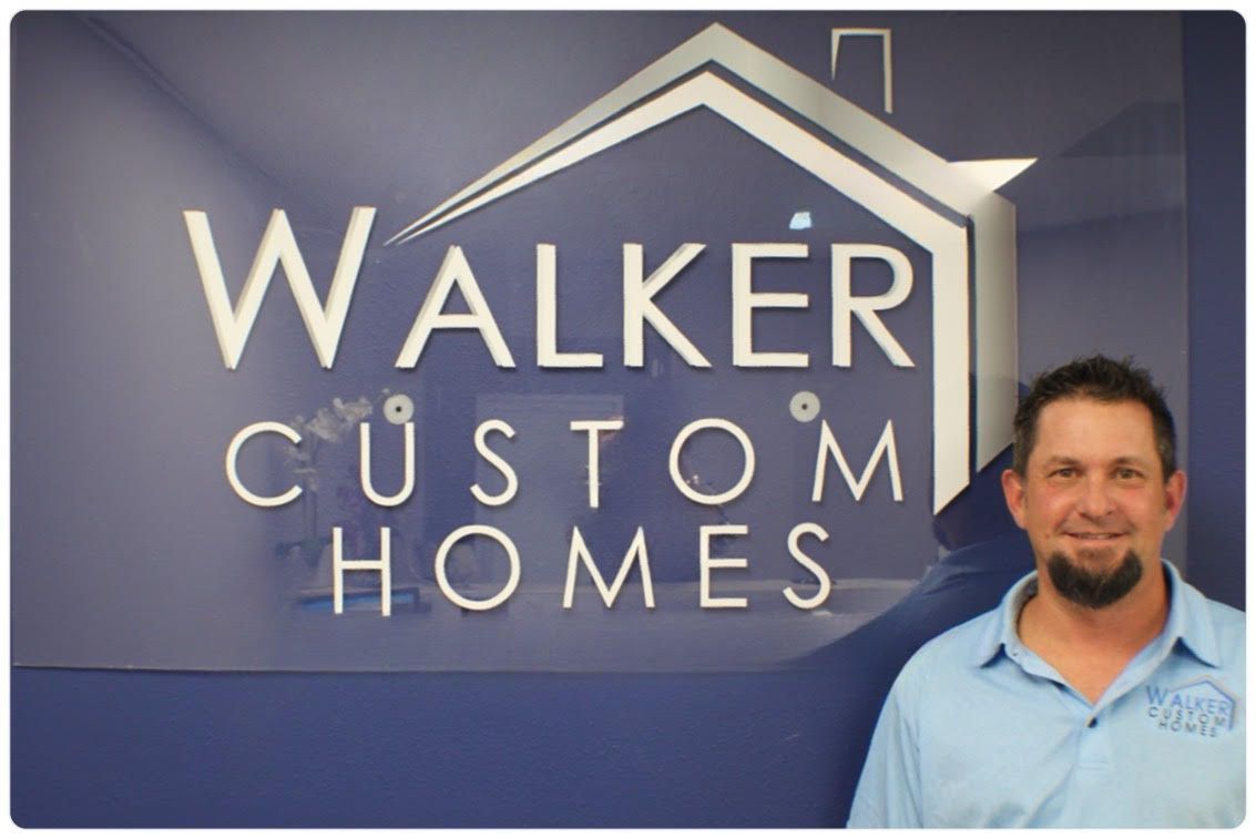 A man stands in front of a sign for walker custom homes