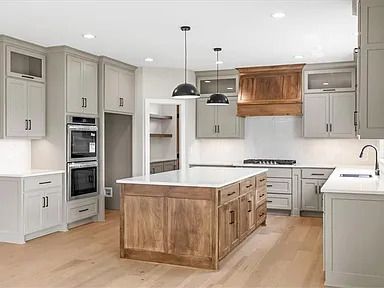 Modern kitchen with light gray cabinets, wood island, and stainless steel appliances.