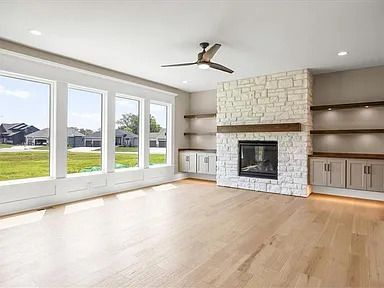 Bright living room with fireplace, windows, light wood floor, and built-in shelves.