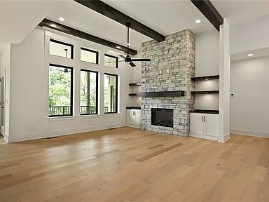 A living room with hardwood floors , a stone fireplace , and a ceiling fan.