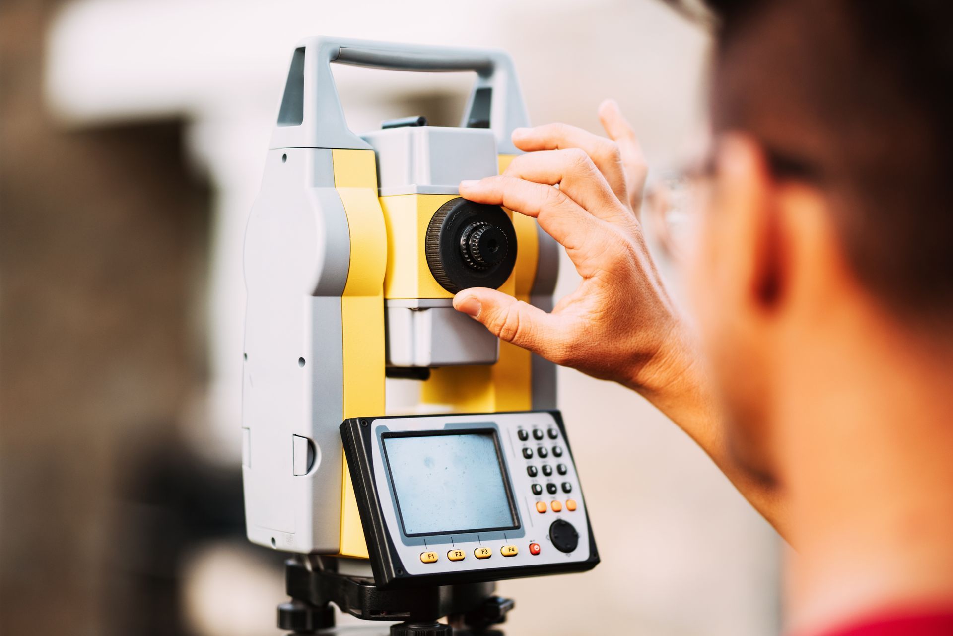 Person operating a yellow and gray surveying theodolite.
